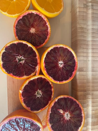 Kundenbild von aufgeschnittenen Bio-Mini-Orangen, die tiefrotes und oranges Fruchtfleisch auf einem Holzbrett zeigen.