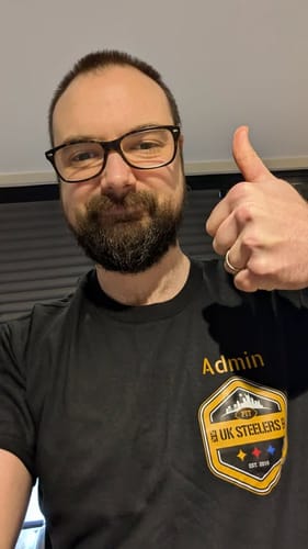 Reviewer wearing a black unisex t-shirt with a yellow 'Admin' and 'UK Steelers' logo, giving a thumbs-up.