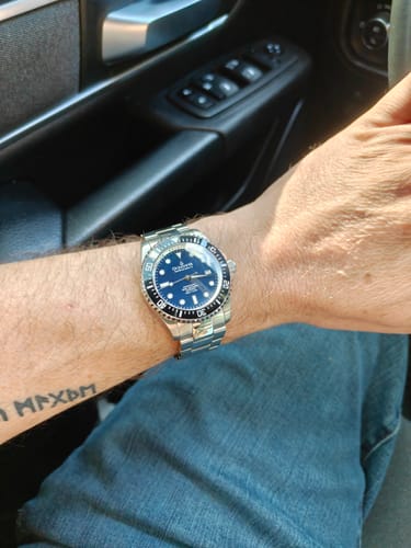 A reviewer wearing the Oceaneva Deep Marine Explorer II watch, showing the navy blue dial and stainless steel bracelet on their wrist.