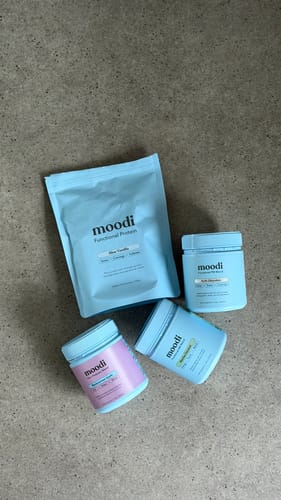 Reviewer's collection of Moodi products, including the Mylk Chocolate blend from the AM-PM bundle, on a counter.