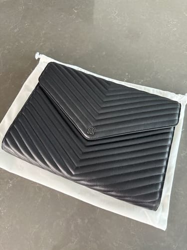 Customer's black Signature Clutch with chevron quilting, shown resting on its white dust bag.