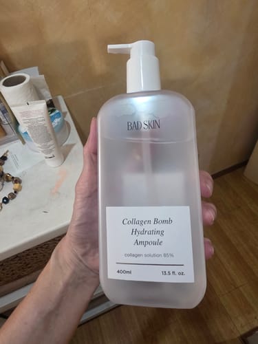 Reviewer holding the large, iridescent bottle of Bad Skin Collagen Bomb Hydrating Ampoule.