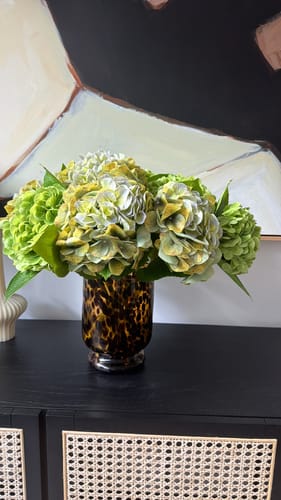 Customer's lifelike Olive Green Hydrangeas arranged in a patterned vase on a black sideboard.