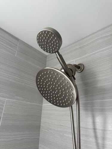 Customer's installed Dual Shower Head Set with a metal finish shown against a grey tiled wall.