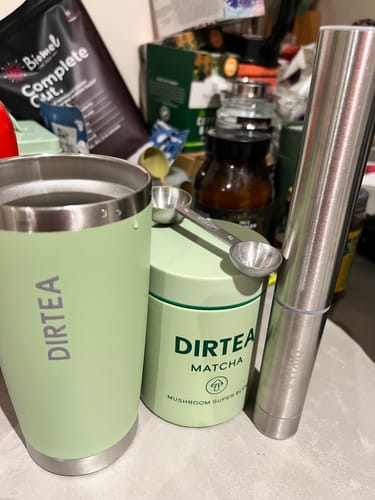 Customer's DIRTEA Matcha tin next to a matching green tumbler and frother on a cluttered kitchen counter.