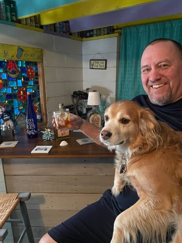 Reviewer smiling while holding their dog and a glass of whiskey from their successfully delivered shipment.