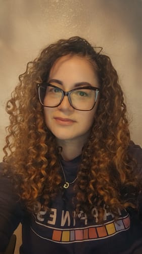 Reviewer with glasses showing off their long, brown hair styled in defined beach curls.