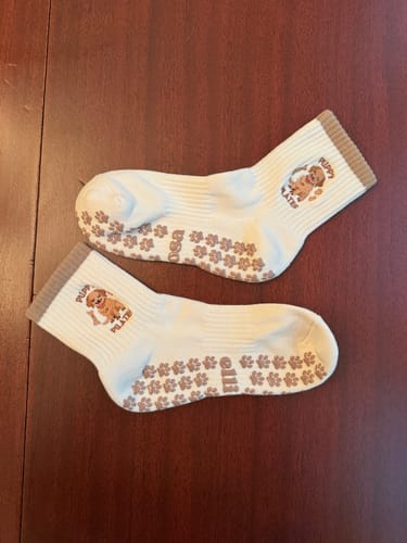 Reviewer's pair of white Puppy Pilates socks laid flat, showing the brown paw print grips on the soles.