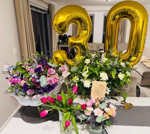 Reviewer's vibrant Luxury Lavender Garden Bouquet on a table with other flowers and '30' birthday balloons in a home setting.