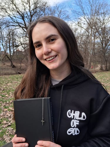 Reviewer holding a closed book, showing the Verse-Accent Bookmark's delicate chain and cross charm.