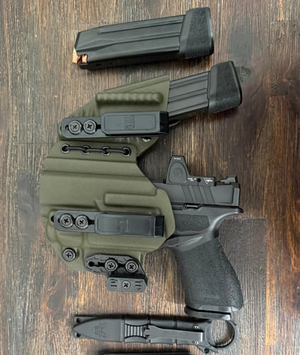 Customer's olive green AXIS ELITE holster laid out on a wood surface with a pistol, magazine, and knife.