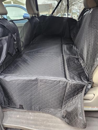 Reviewer's black waterproof hammock cover installed in the back seat of a van, showing its full coverage.