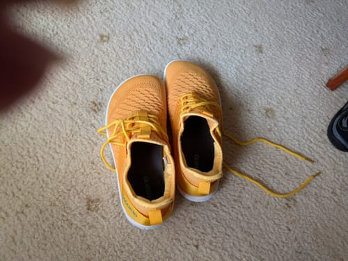 Customer's pair of orange Go I Casual Barefoot Shoes resting on a carpet.