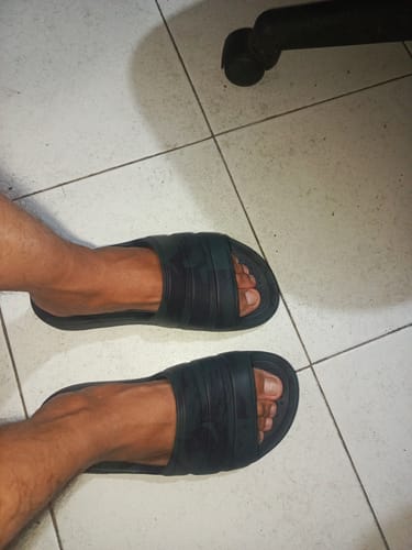 A customer's feet wearing the black adidas Adilette Flow slides indoors on a tiled floor.