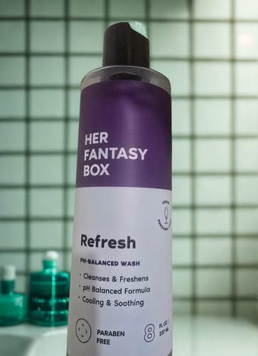 Customer's bottle of Refresh Plant Based Intimate Body Wash with a purple and white label, set in a bathroom.