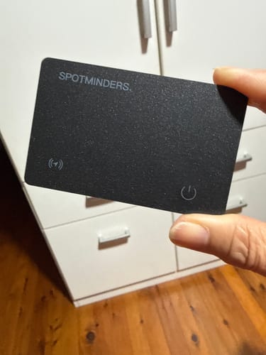 Customer holding the thin, black SPOTMINDERS Tracking Card between their fingers in a room.