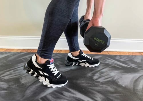 Customer wearing the black and white Ortho Step 2.0 sneakers while holding a dumbbell on a mat.