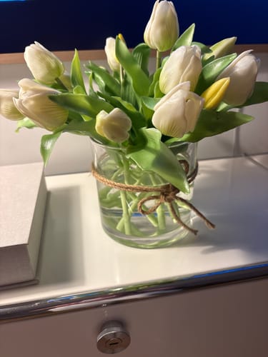 Reviewer's bunch of white short-stem tulips displayed in a small glass vase on a white tabletop.