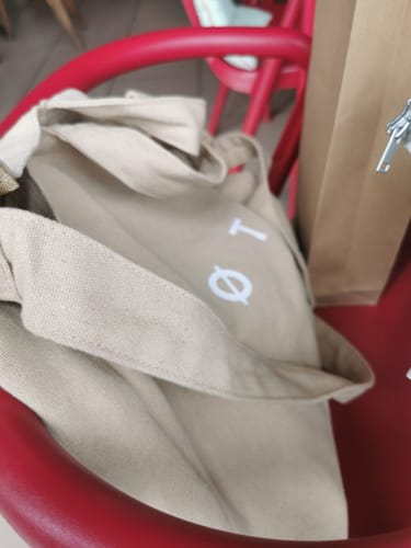 Partial view of a reviewer's beige TØTE Bag resting on a red chair, with the white logo visible.