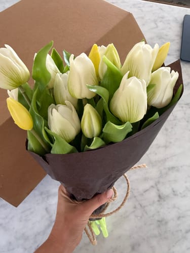 Customer holding a fresh bunch of white short stem tulips wrapped in brown paper.