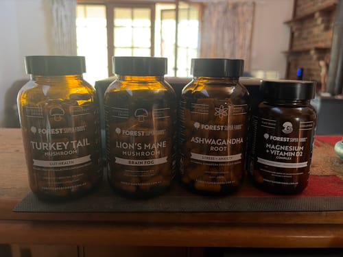 Customer's amber bottle of Lion's Mane Mushroom Capsules lined up on a table with other Forest Super Foods supplements.