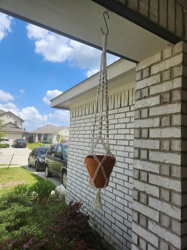 Reviewer's completed macrame plant hanger from their DIY craft box, holding a terracotta pot on a porch.