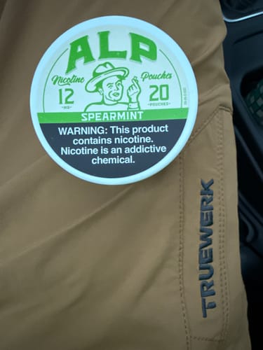 Customer's tin of ALP Spearmint Nicotine Pouches resting on a pair of brown pants.