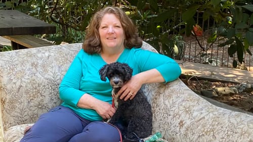 Reviewer sitting on a couch outdoors with a dog, wearing the bright Elena 3/4 Sleeve V Neck top.