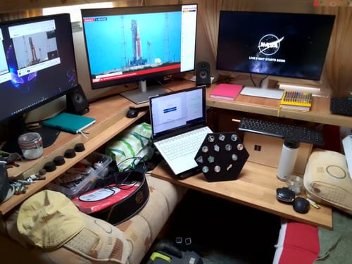 Customer's SpaceX Starship Flight Pin Collection on its display mount, shown on a desk with monitors displaying a rocket launch.