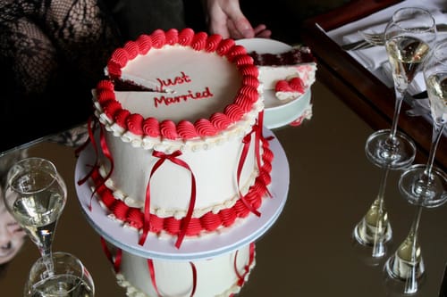 Customer's Bespoke Vintage Cake with 'Just Married' in red icing. A hand serves a red velvet slice on a mirrored table.