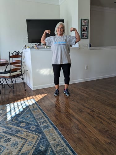 Reviewer flexing her biceps at home, showing the results of taking V1X PRODIGY pre-workout.