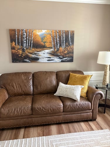 Customer's The Birchwood Stream canvas print hanging on a wall above a brown leather sofa in a living room.