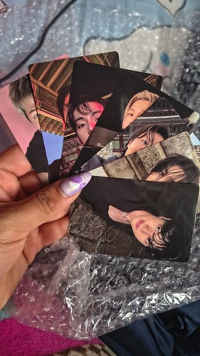Customer's hand holding a fan of unreleased photocards from the BTS ARIRANG 5TH ALBUM set over bubble wrap.