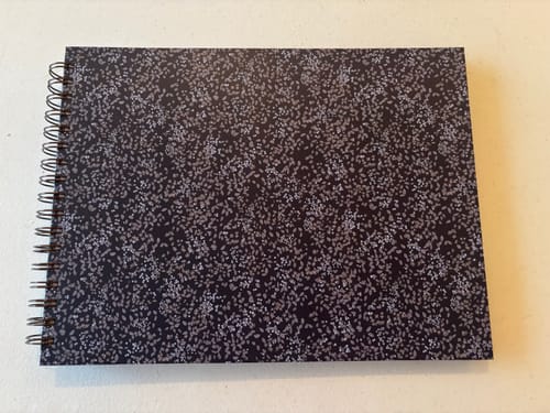 Customer's closed Nancy Planner with a black and white speckled cover lying on a flat surface.
