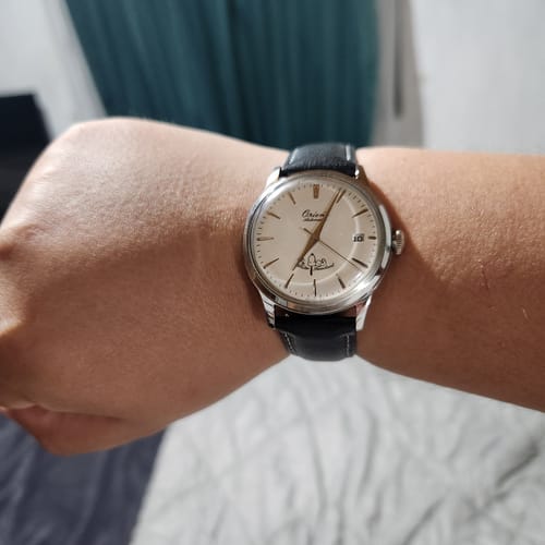 Cliente mostrando el reloj Orient Bambino edición Peanuts en la muñeca. El reloj tiene esfera blanca y correa de cuero negra.