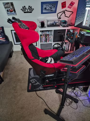 Customer's red and black racing simulator cockpit with a bucket seat set up in a room.