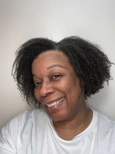 Reviewer smiling, showing moisturized, natural curly hair after using the BOOST Leave-In Detangling & Refreshing Spray.