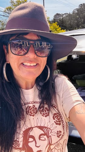 Reviewer smiling outdoors while wearing the Unisex Sand Grito Tee with a large hat and sunglasses.
