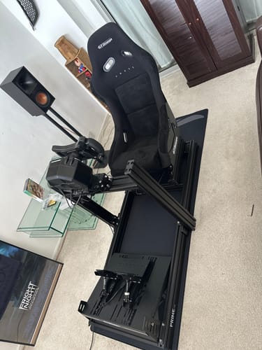 Customer's fully assembled black PRIME Lite Cockpit with a racing seat, wheel, and pedals on a floor mat.