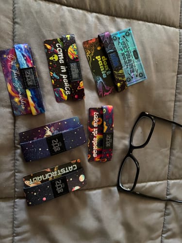 Customer's collection of seven space-themed Mystery Club+ bracelets, including a holographic ultrarare design, on a bed.