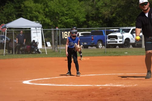 Reviewer's child wearing the NEO Softball Fielder's Mask, in a ready position on a softball field.