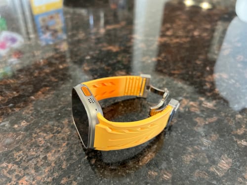 Customer's faded yellow fluoro rubber strap for an Apple Watch, with the butterfly clasp open, sitting on a countertop.