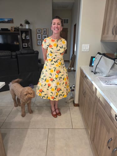 Reviewer smiling while wearing the yellow 1950s-style dress with a citrus print in her kitchen.