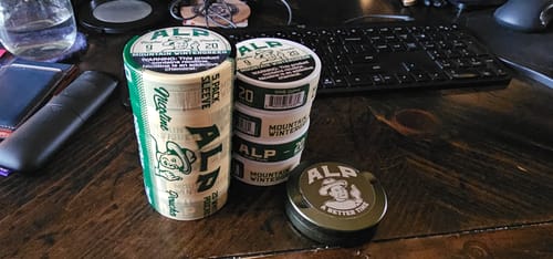 Customer's sleeve and several cans of Mountain Wintergreen Nicotine Pouches arranged on a wooden desk.