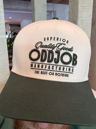Customer showing the front of their two-tone Big Structured A-Frame Hat with a dark green brim and embroidered logo.