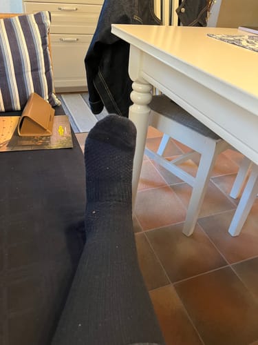 En kund vilar med en svart Diasocks stödstrumpa på foten i hemmiljö.