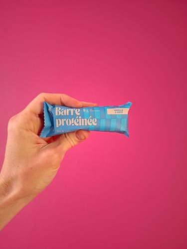 Un client tient une barre protéinée Bioproduct saveur vanille-coco dans son emballage bleu.