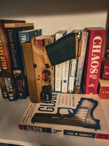 Reviewer's black Raid Tape wrapped around the grip of a tan handgun, which is resting on a bookshelf in front of several books.