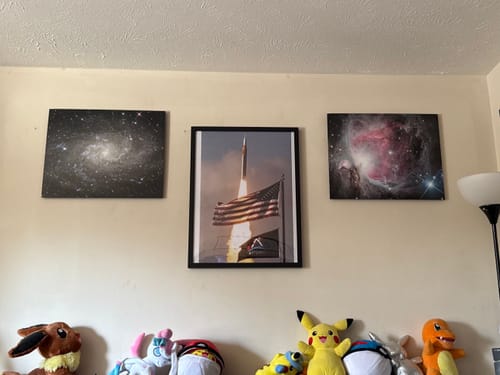 Reviewer's "Four Souls, One Rocket" framed print hanging on a wall between two other pieces of space art.