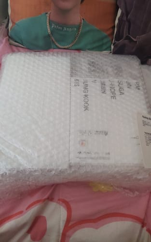 Customer's BTS ARIRANG 5th album box, still sealed in protective bubble wrap, lying on a pink bedspread.
